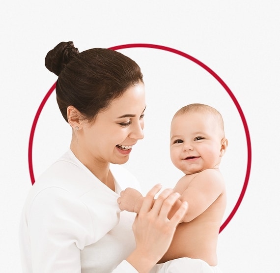 Среќна млада мајка, облечена во бела кошула го држи своето насмеано бебе
